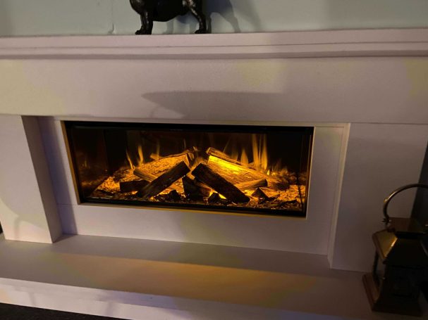 An electric fireplace with glowing logs and flames, set in a modern white mantle.