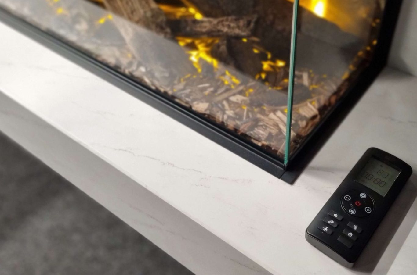 A close-up of a remote control next to a modern British Fires glass fireplace