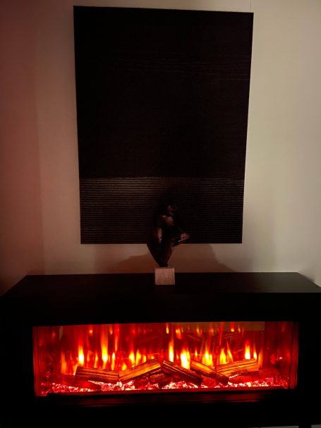 A modern electric fireplace with glowing red lights and a dark abstract wall art above it.