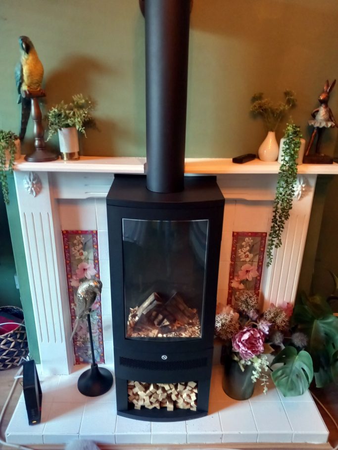 A modern black wood-burning stove on a white mantelpiece with decorative plants and figurines.