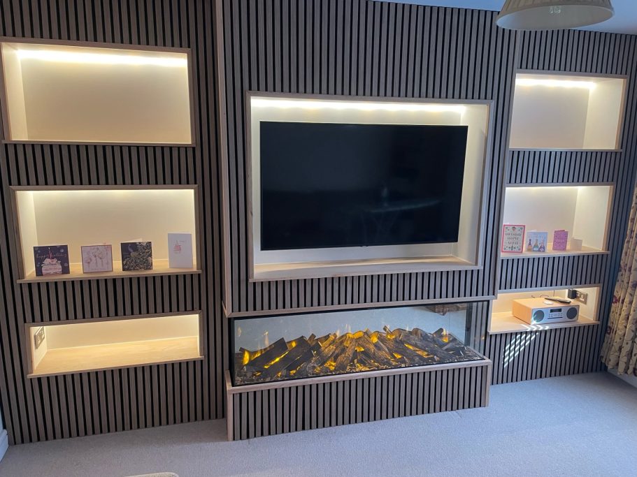 Modern living room with a sleek TV unit and illuminated shelves displaying books. With a british fires electric fireplace