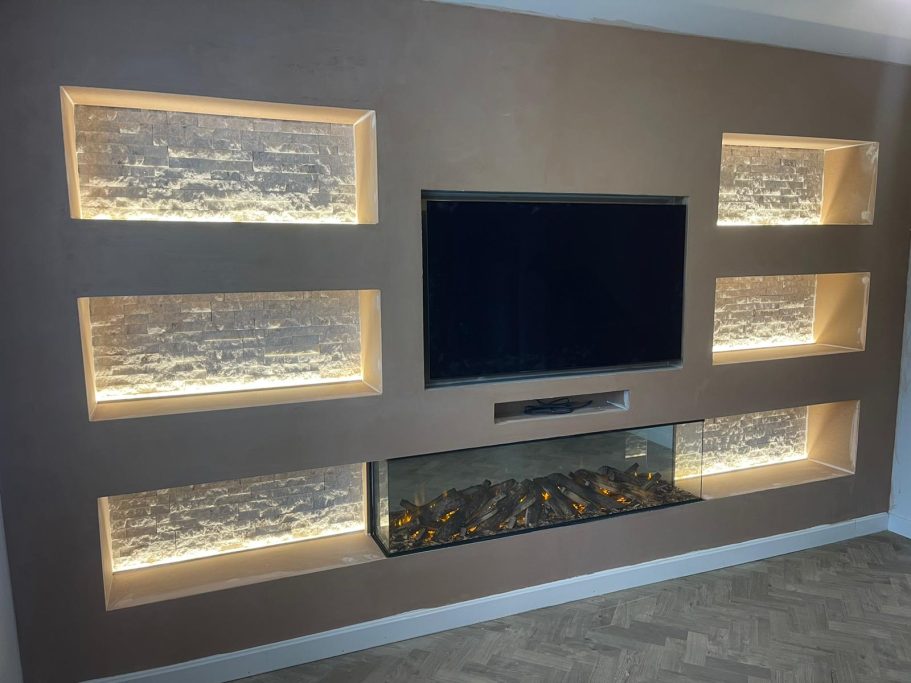Modern living room wall featuring a TV, illuminated shelves, and an integrated electric fireplace.
