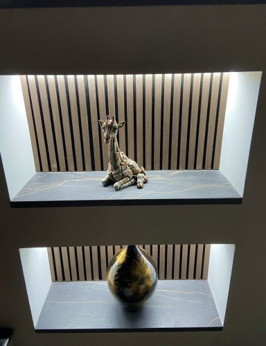 A decorative giraffe sculpture on a shelf above a vase with a glossy finish.