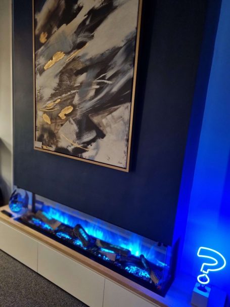 A modern room with a blue-lit Flamerite electric fire, abstract artwork, and a whimsical neon question mark.
