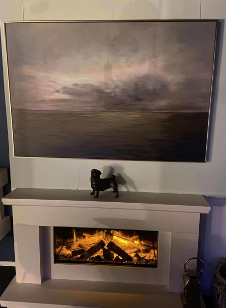 A modern fireplace with a glowing display, beneath a large abstract landscape painting.